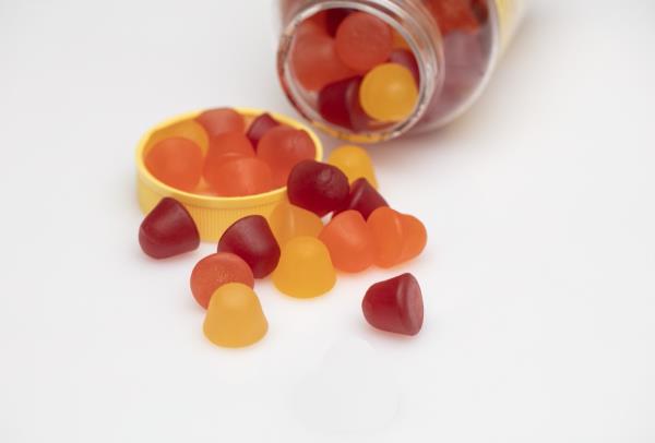 gummy vitamins being poured out of a bottle o<em></em>nto white surface