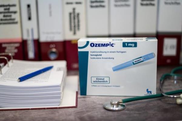 A Drug box of Ozempic co<em></em>ntaining Semaglutide for treatment of type 2 diabetes and long-term weight management on a table and in the background different medical books.