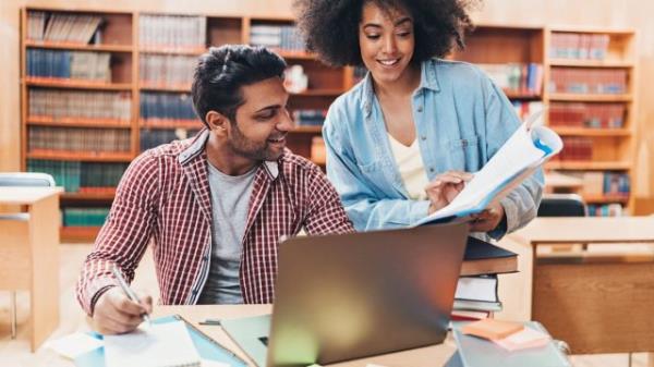 friend explaining book to classmate in library