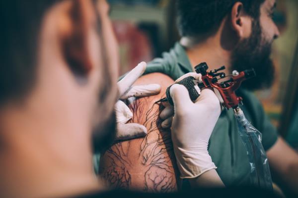 Two men, tattoo artist tattooing a man's arm in his tattoo studio.